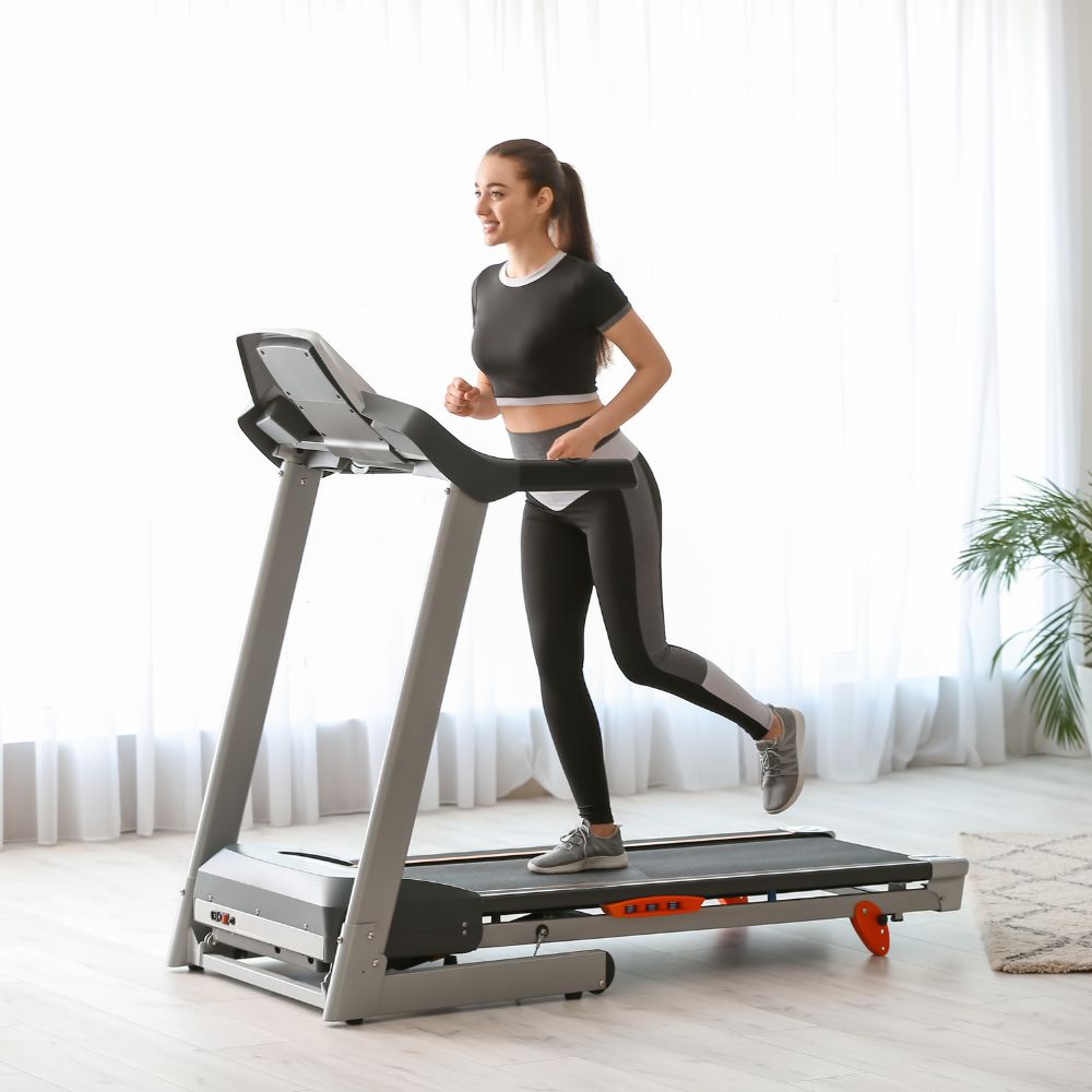 Woman running on a treadmill in a bright room with white curtains.