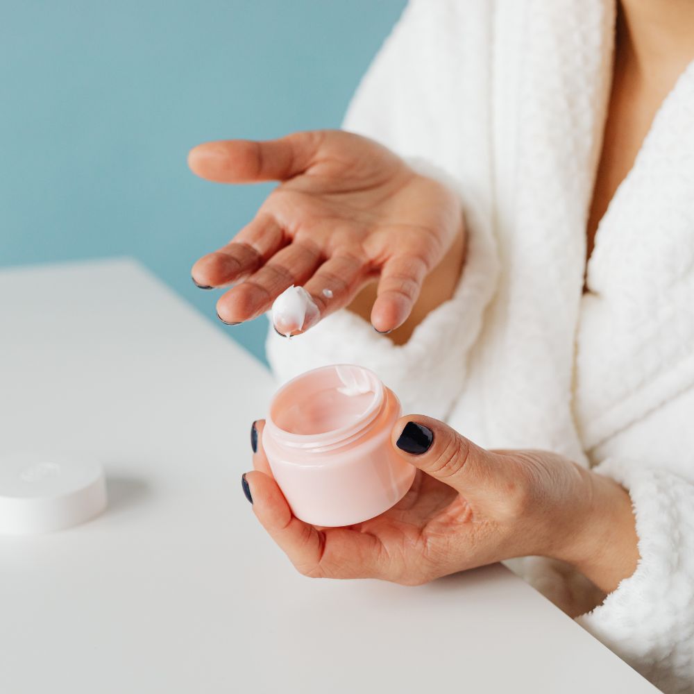 Person applying cream from a pink jar with a blue background