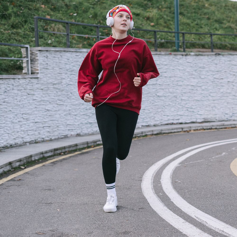 Person running on a track wearing a red sweatshirt and black leggings.